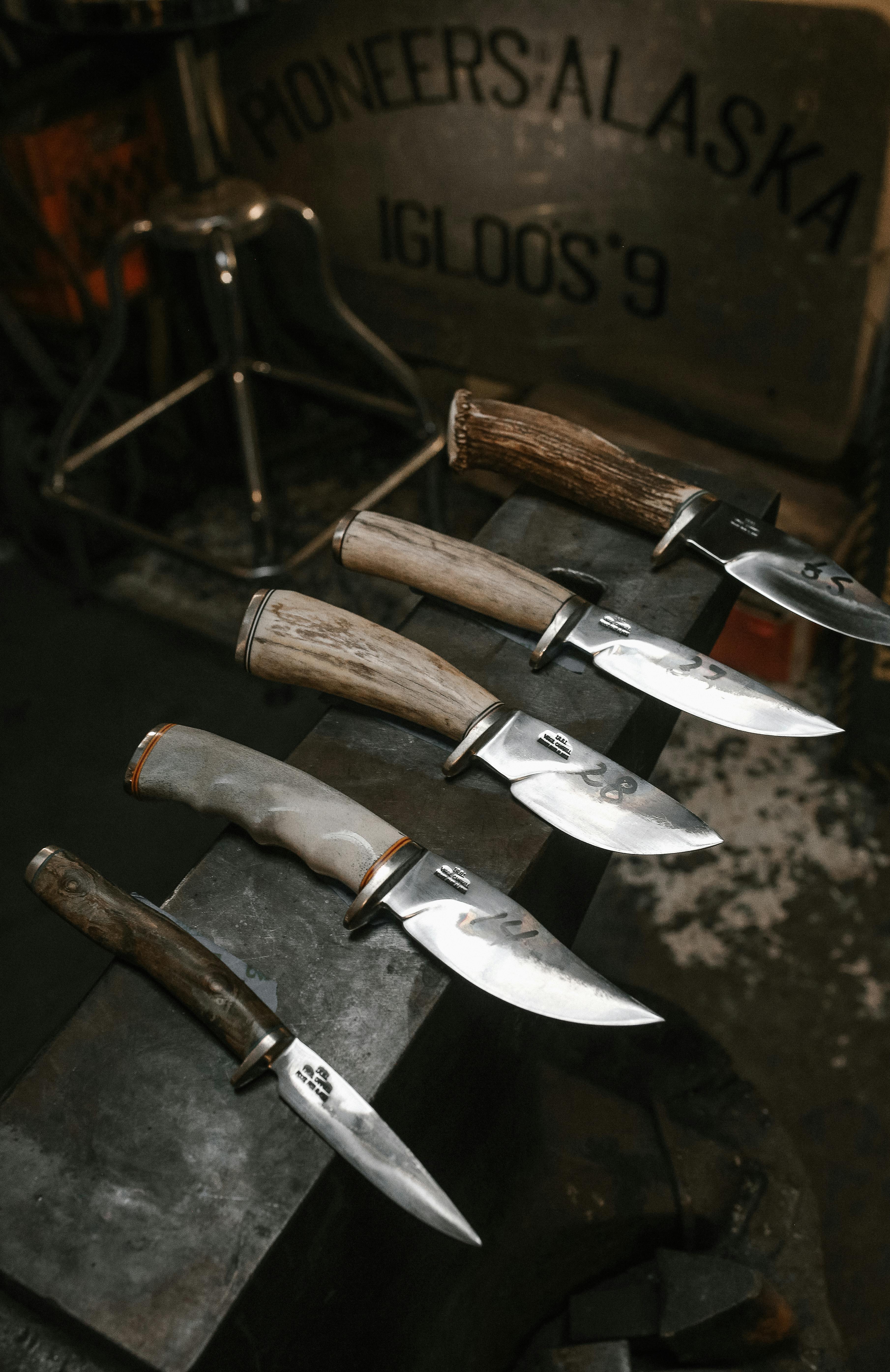 Five handcrafted knives with antler and wood handles resting on a steel anvil in a forge workshop